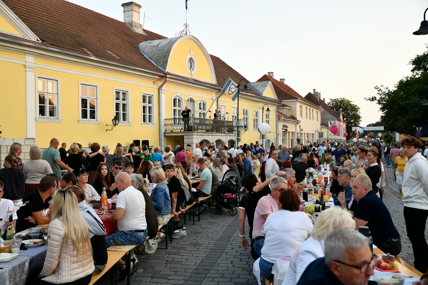 Persone che cenano e ballano a una vivace festa di strada al tramonto.