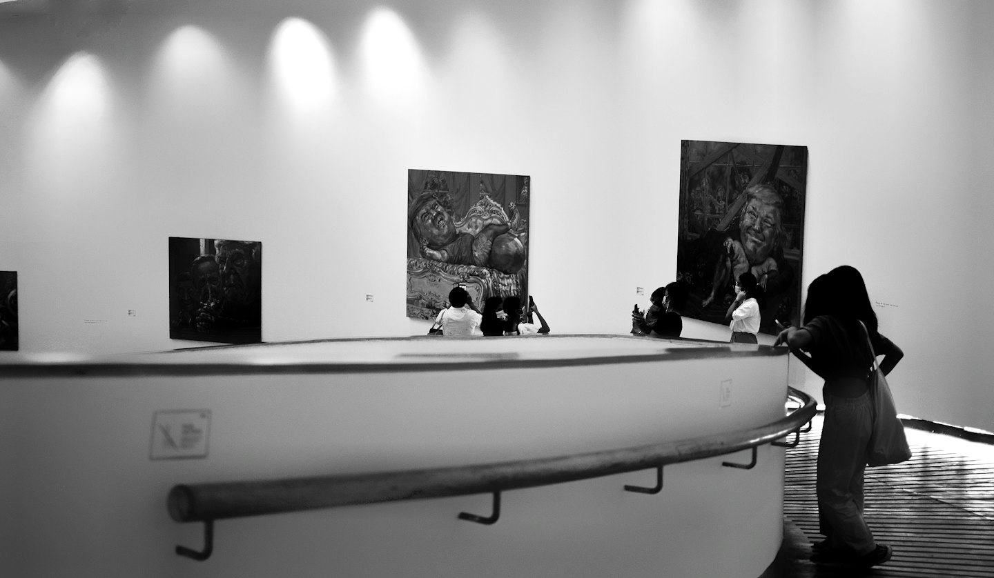 Visitatori di una galleria osservano dipinti contemporanei esposti su pareti bianche.